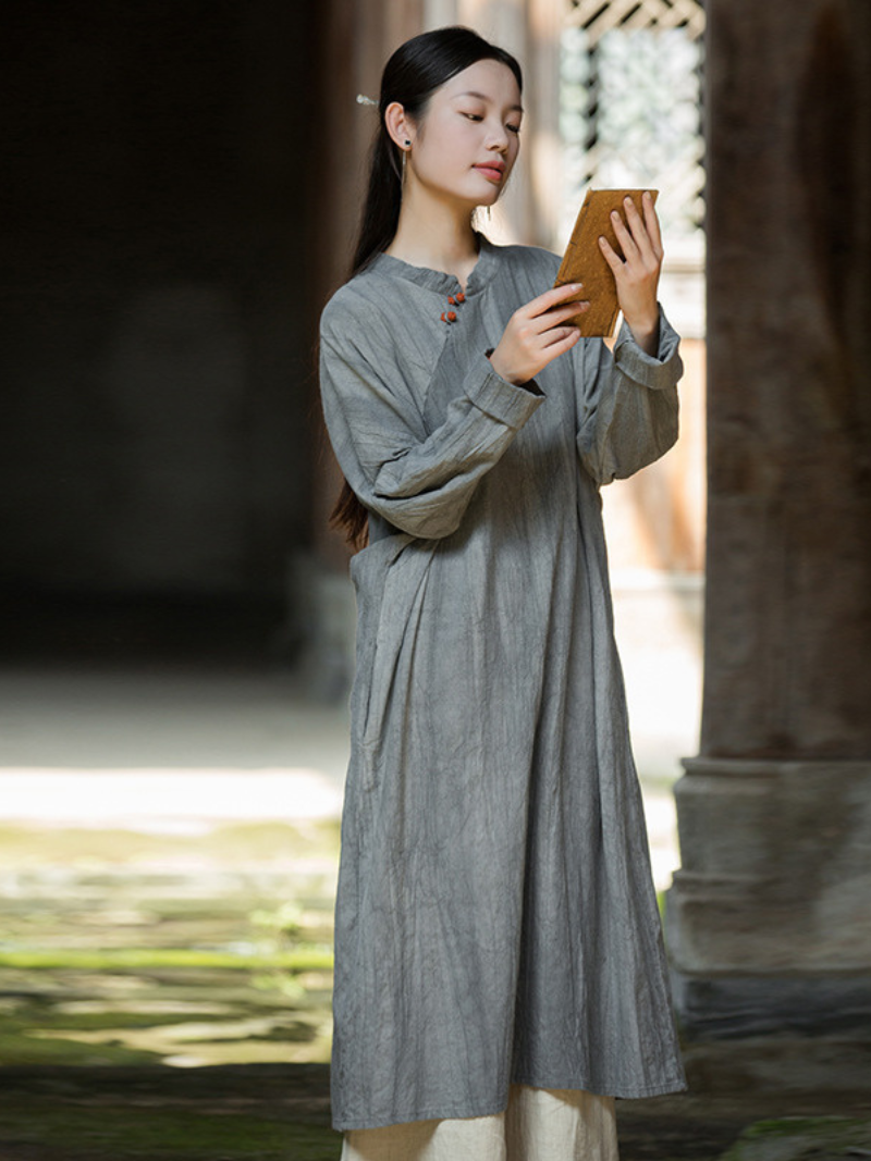 Woman in a long gray dress holding a wooden object outdoors.