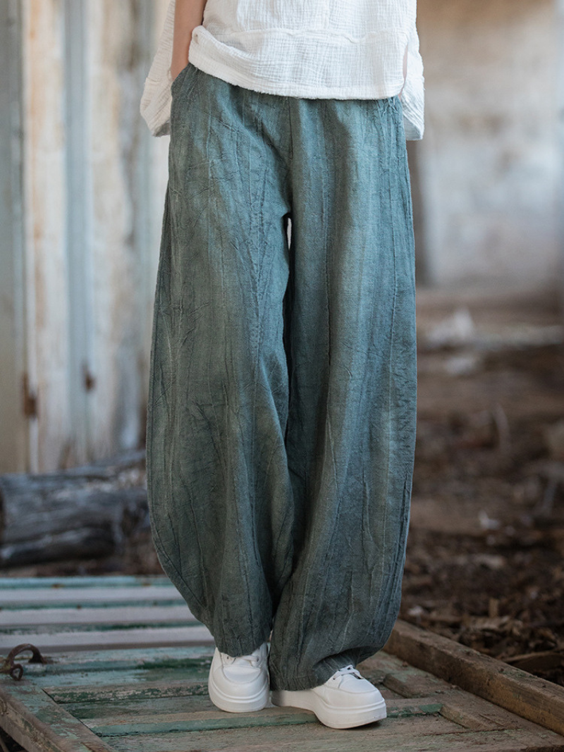  wearing teal wide-leg pants and white shoes in a rustic setting