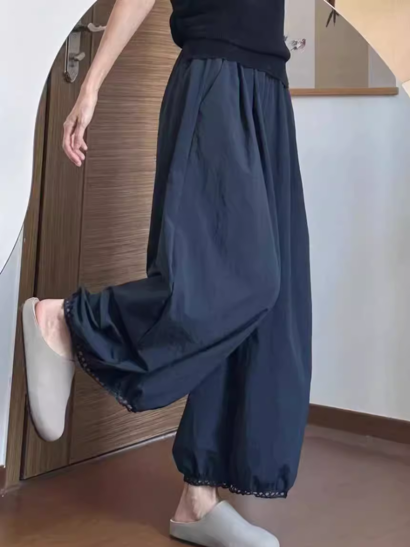 Person wearing dark blue wide-leg pants and white shoes in a room with wooden flooring.