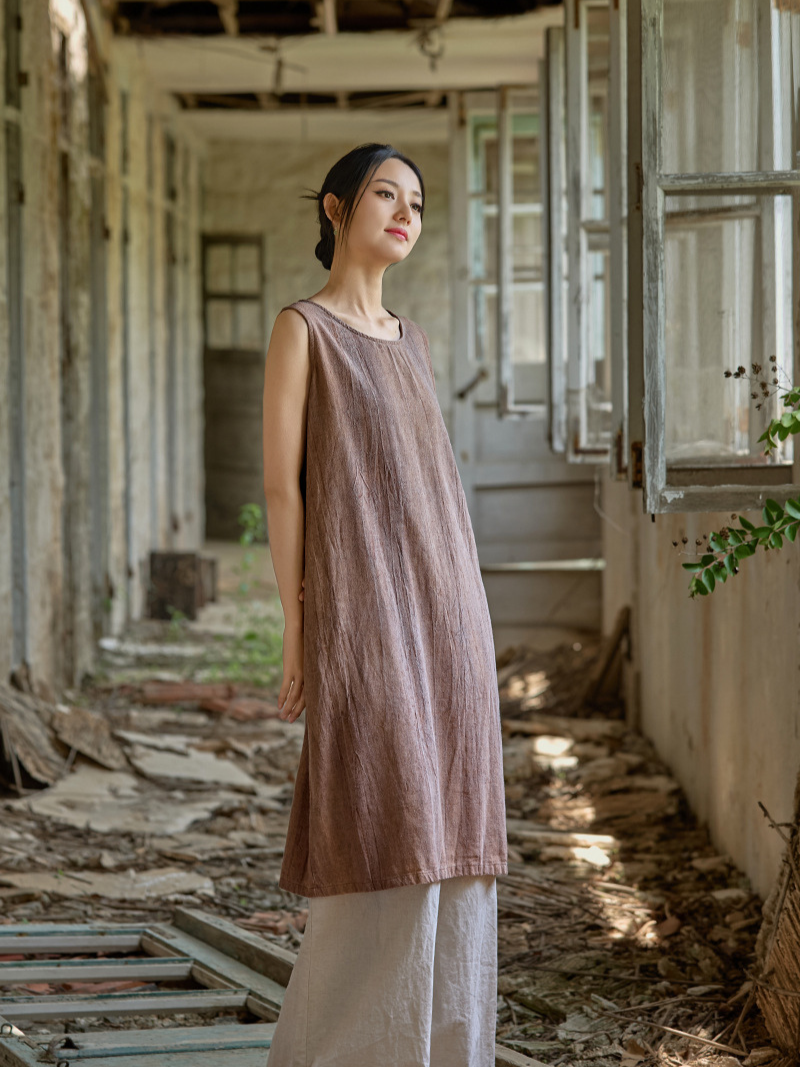 Woman in a brown dress standing in an abandoned building with debris on the floor.