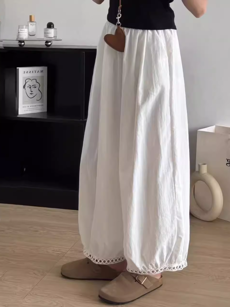 Person wearing white wide-leg pants with lace trim in a minimalistic room.