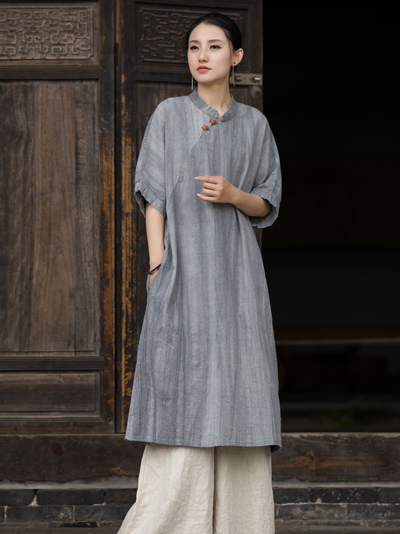 Woman wearing a gray traditional outfit standing in front of a wooden door.