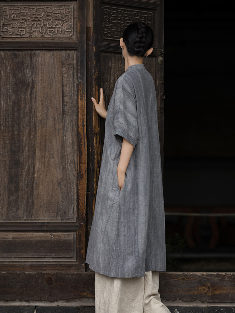 Person wearing a long gray garment standing in front of a wooden door.