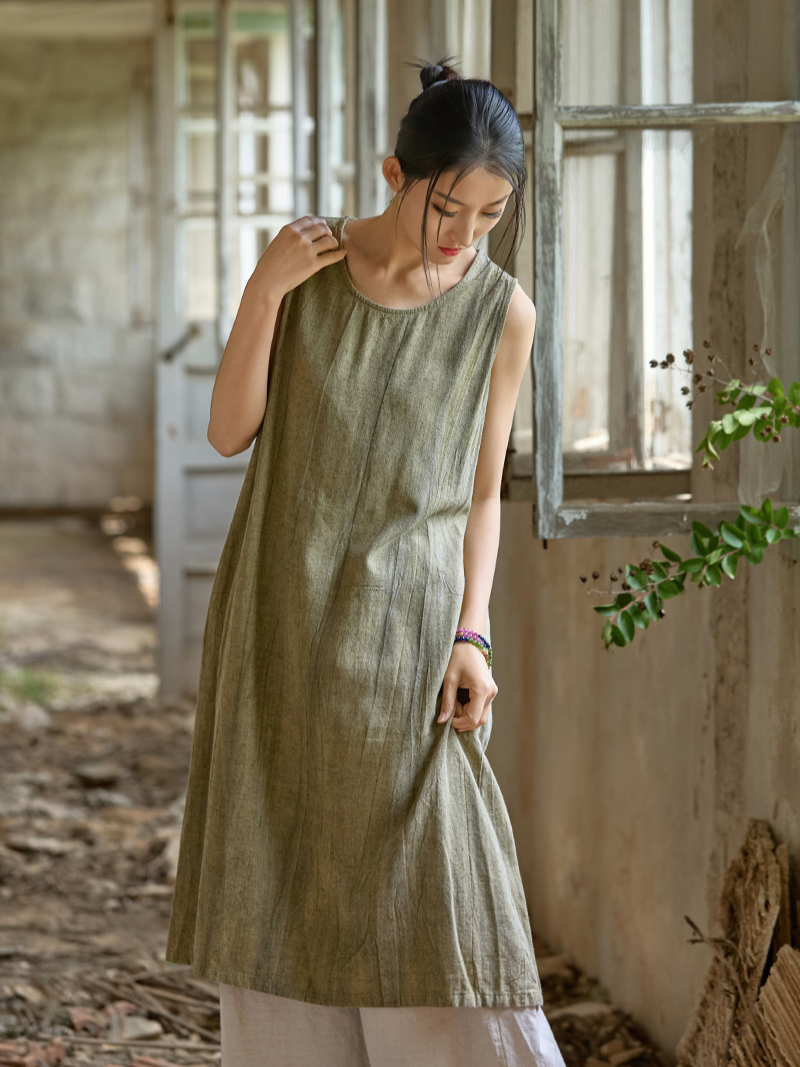 Woman wearing a green dress standing in a rustic indoor setting with wooden walls and a window.