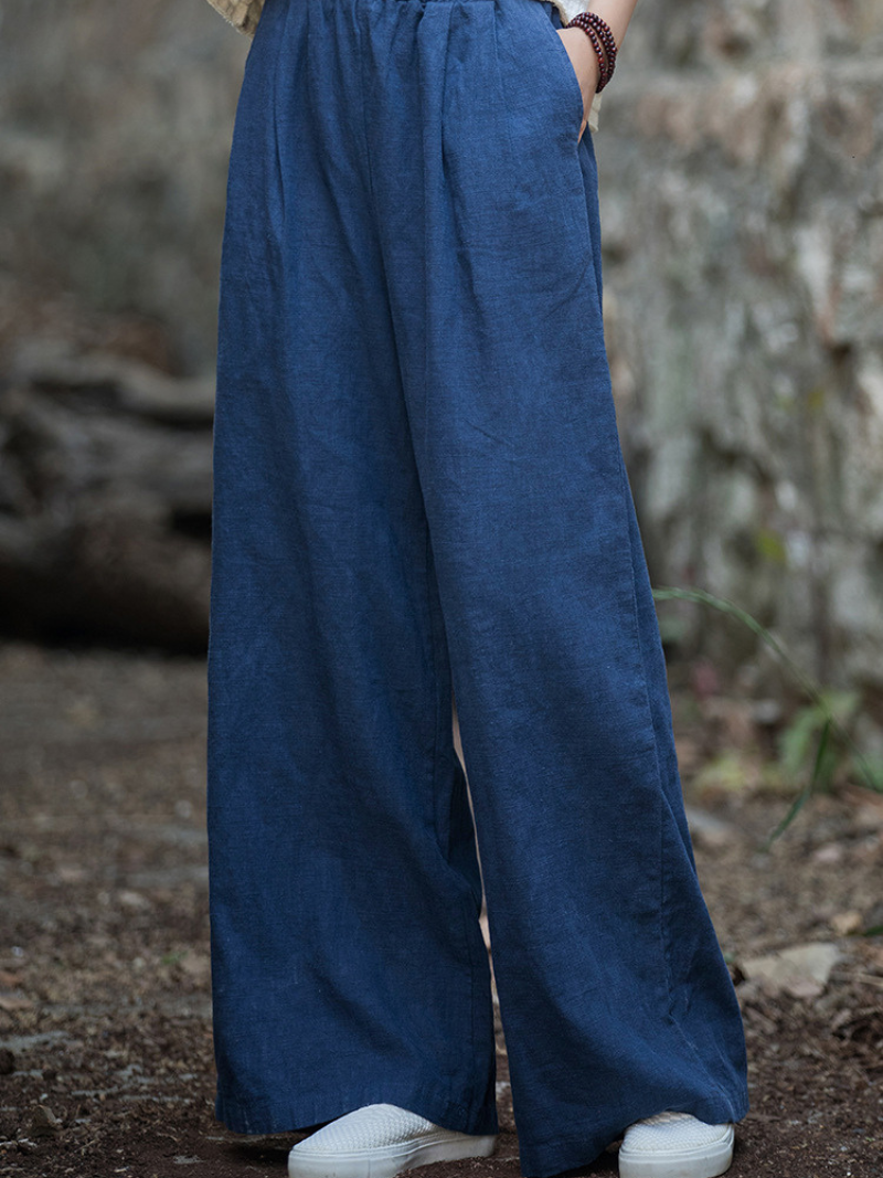 Person wearing blue wide-leg pants standing against a stone wall.