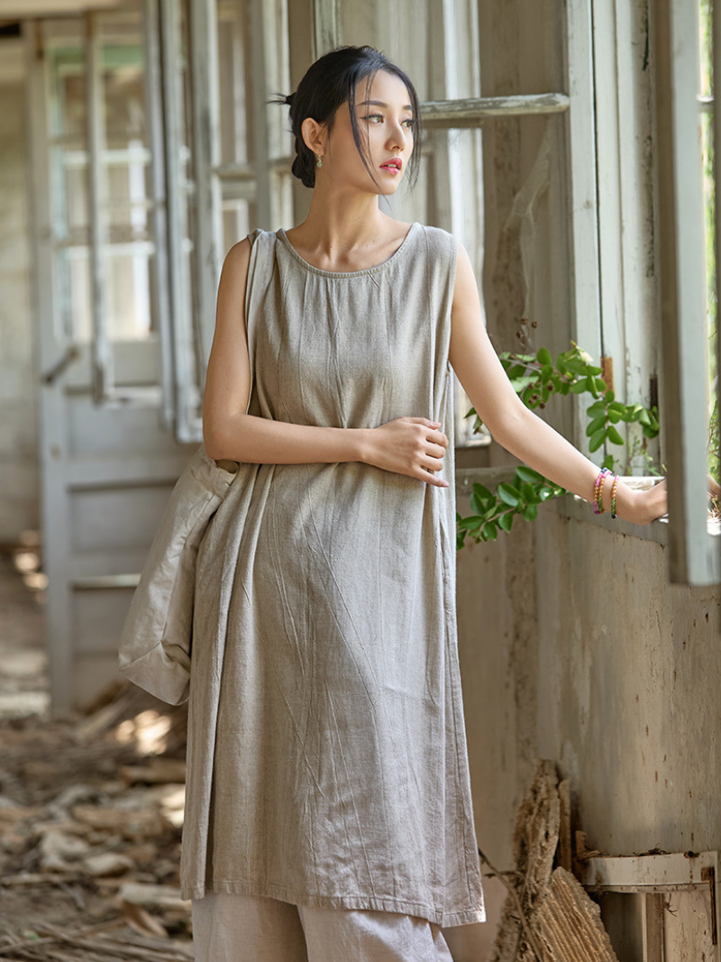 Woman wearing a beige dress standing in a rustic indoor setting with plants.