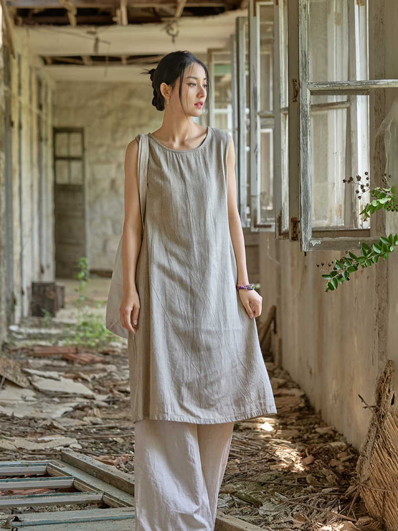 Woman in a beige dress standing in an abandoned building with sunlight filtering through.